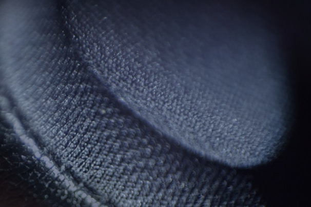 A close-up image focused on a textured surface that appears to be a fabric or textile. The surface is detailed, with visible fibers and a soft sheen, casting shadows that create a sense of depth.