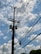 A wooden utility pole with multiple power lines stretches across a partly cloudy blue sky. Several transformers and a street lamp are attached to the pole.