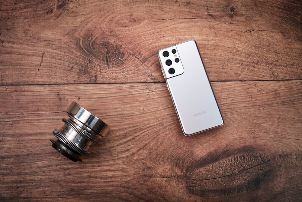 a white cell phone and a black and silver camera on a wooden surface