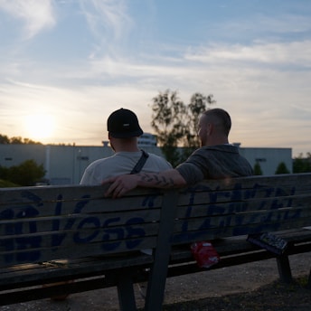 Two men sit on a bench at sunset, symbolizing connection and men’s mental health.