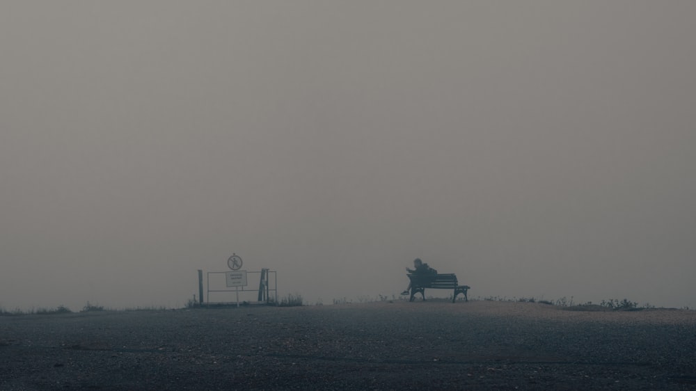 a person sitting on a bench in a field with a sign in the background