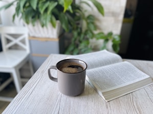 A cozy corner with a steaming cup of coffee next to an open book on a wooden table.
