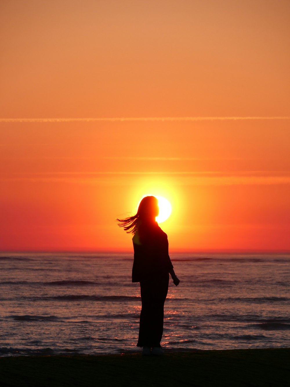 Una persona parada en una playa con la puesta de sol detrás del