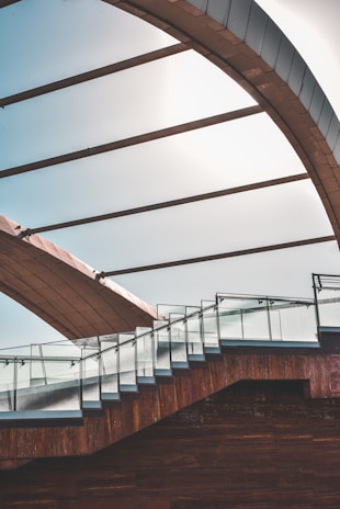 A modern architectural structure featuring a staircase with glass railings and a large curved roof above. The design incorporates clean lines and a mix of materials including glass and wood, creating a visually striking contrast.