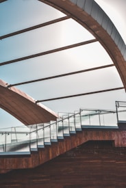 A modern architectural structure featuring a staircase with glass railings and a large curved roof above. The design incorporates clean lines and a mix of materials including glass and wood, creating a visually striking contrast.