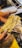 A person with flour-dusted hands is holding a bunch of freshly made pasta. The background shows a countertop sprinkled with flour and various kitchen tools.