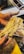 A person with flour-dusted hands is holding a bunch of freshly made pasta. The background shows a countertop sprinkled with flour and various kitchen tools.