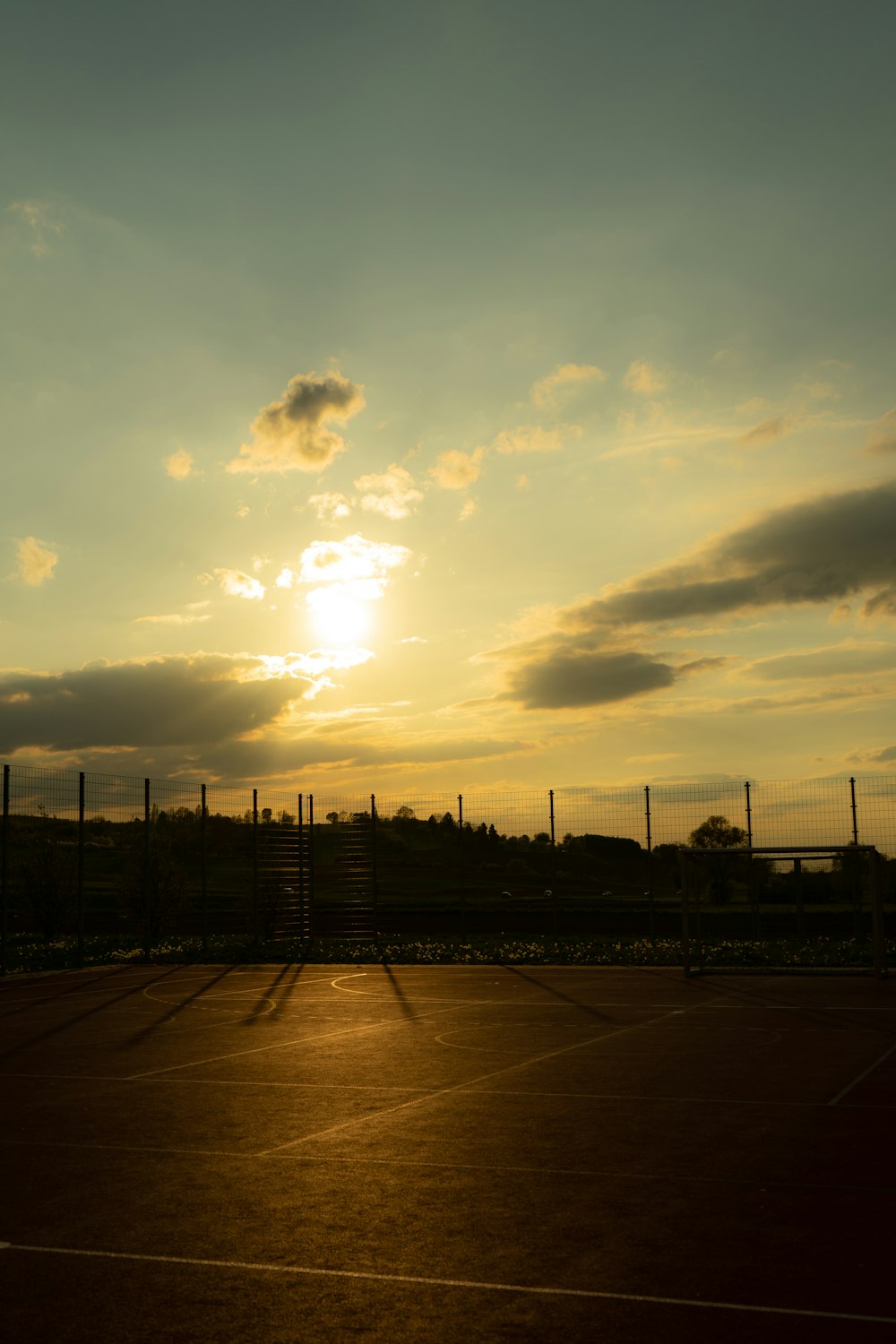 a tennis court with a fence and a sunset