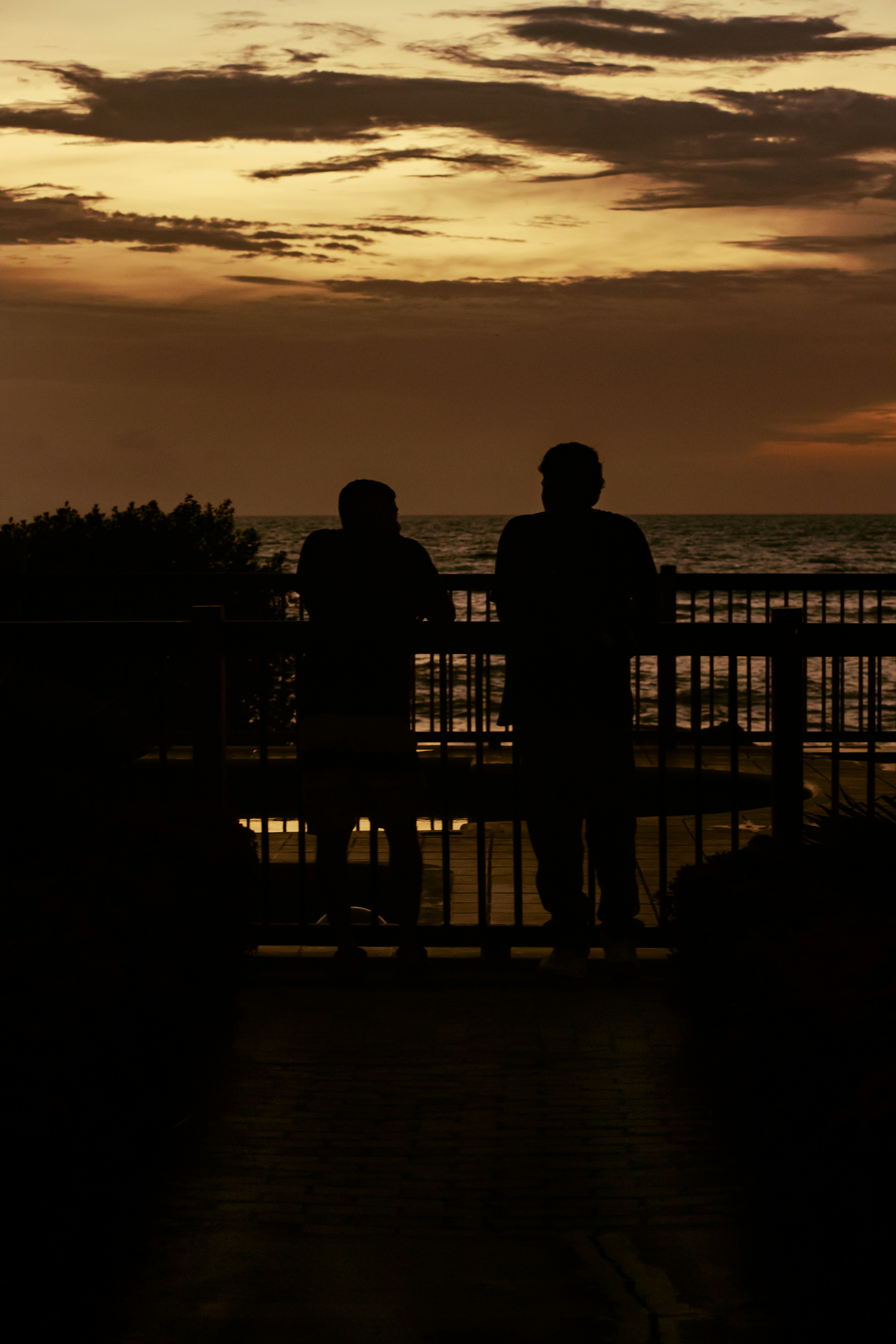 a couple of people sitting on a bench looking at the sunset