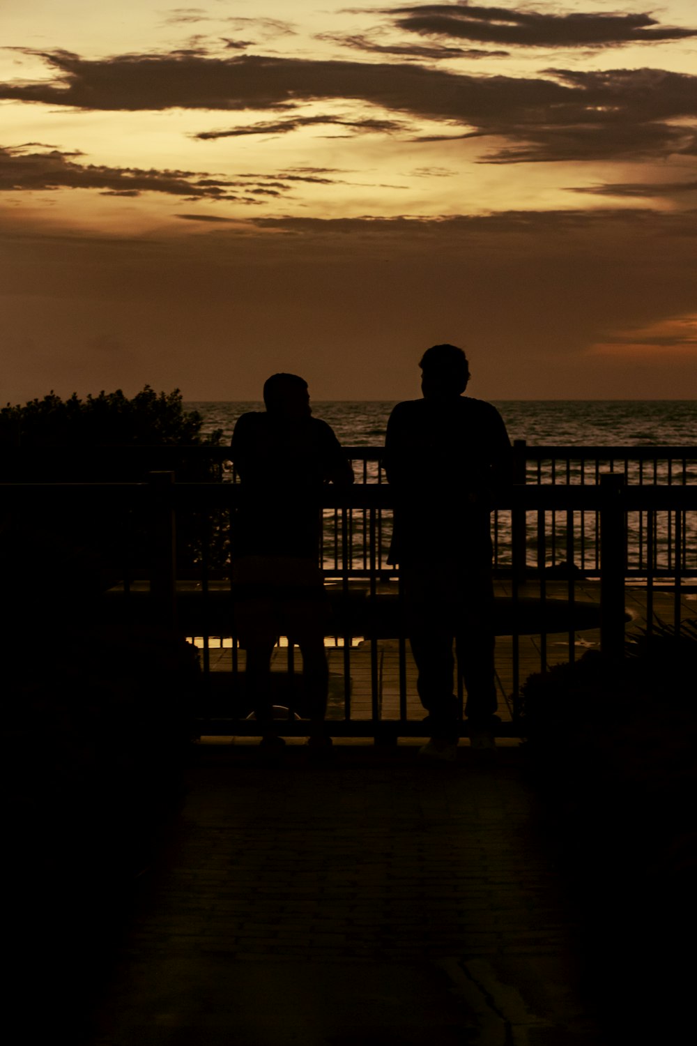 um casal de pessoas sentadas em um banco olhando para o pôr do sol