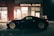 A sleek black sports car is parked outside a medical clinic at night. The building is illuminated by a red neon sign that reads 'MEDICAL CLINIC'. The environment appears quiet and empty, with a dimly lit parking area and subtle reflections on the car's surface.