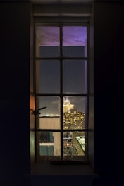 Evening view through a big hotel window revealing the glowing cityscape beyond.