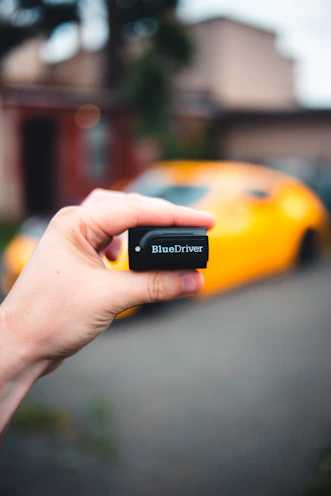 Hands holding a 3D printed diagnostic tool with a car dashboard in the background.