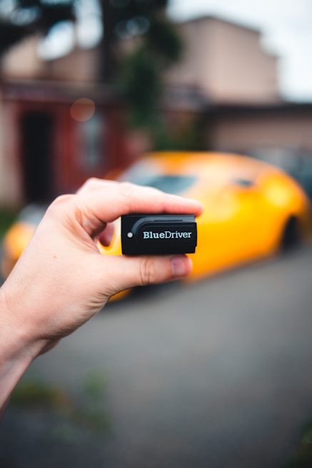 Hands holding a diagnostic tool connected to a vehicle’s electrical system.