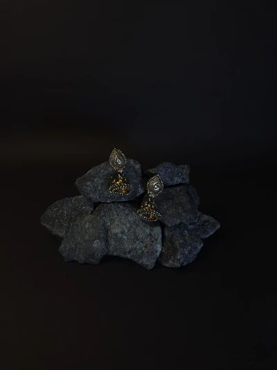 A pair of earrings crafted from rough-cut garnet stones and darkened silver, displayed against a backdrop of stormy ocean waves.