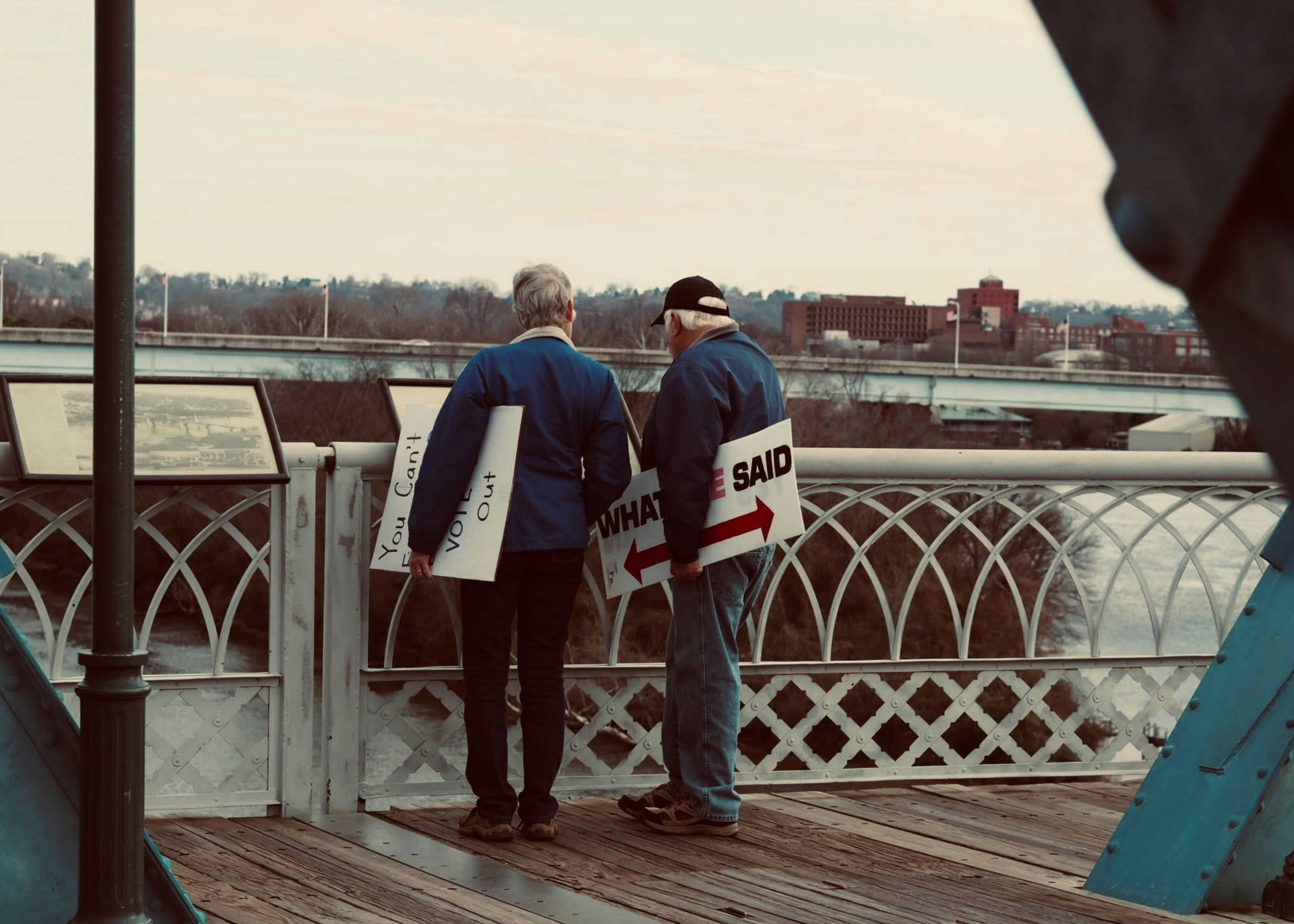 Un couple d’hommes debout sur un pont regardant un panneau