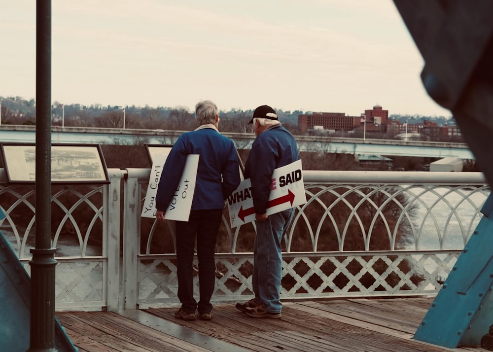 a couple of men standing on a deck looking at a sign