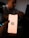 A person holds a smartphone with the Notion logo on the screen. The background is dimly lit, with a blurred figure sitting at a desk possibly using a laptop.