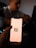 A person holds a smartphone with the Notion logo on the screen. The background is dimly lit, with a blurred figure sitting at a desk possibly using a laptop.