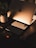 A sleek workspace setup with a laptop displaying an illuminated logo, two smartphones, a smartwatch, and a bank card arranged neatly. A potted plant adds a touch of nature, and the warm lighting creates a cozy atmosphere.