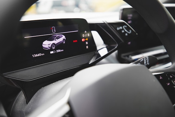 The interior view of a modern car's dashboard featuring a digital display. The screen shows a graphic representation of a vehicle with mileage and distance information displayed. A steering wheel and other dashboard controls are partially visible.