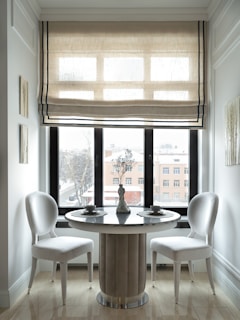 a dining table with chairs and a window with blinds