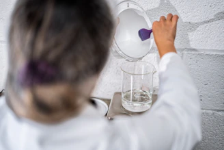 Close-up of a scientist in a lab coat carefully mixing chemicals beside high-tech equipment, symbolizing precision and innovation.