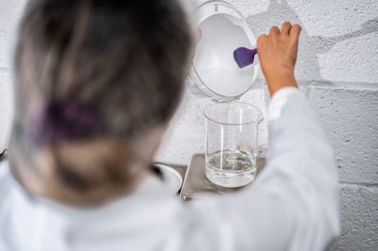 Close-up of a scientist in a lab coat carefully mixing chemicals beside high-tech equipment, symbolizing precision and innovation.