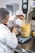 A person wearing a lab coat and hairnet is working with a large industrial mixer in a laboratory setting. They are pouring a substance, possibly corn kernels, into a transparent container filled with a creamy yellow liquid. The equipment is marked with volume measurements and is positioned on a metallic table alongside digital measurement devices.