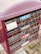 A close-up view of a set of mailboxes with colorful labels in Korean. The mailboxes are housed in a purple casing, and the labels are blue, green, and red. The ground is paved with textured stones, and some small patches of grass are visible.