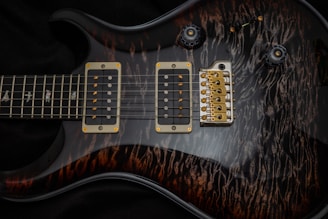 A detailed close-up of an electric guitar showcases the body and strings. The guitar features two humbucker pickups with golden screws. The bridge is metallic with several strings attached, and the fretboard shows intricate inlay designs. The guitar's body has a dark, glossy finish with a unique wood grain pattern.