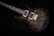 A sleek electric guitar with a richly patterned dark wood finish and detailed inlay work on the fretboard. The guitar's hardware includes dual humbucker pickups and a gold bridge, with control knobs for adjusting sound settings. It rests on a dark fabric background, enhancing the contrast and highlighting the instrument's design.