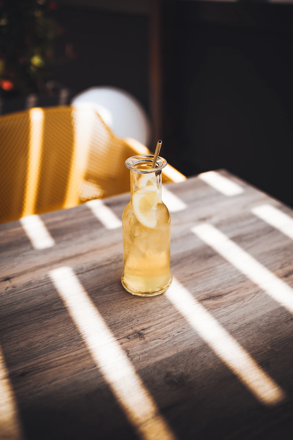 Glass bottle filled with yellow liquid on wooden table with straw protruding nearby