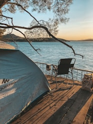 A cozy tent pitched beside a calm lake at sunset with soft golden light.