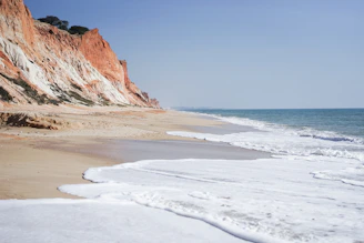 Soft waves lap against a pristine sandy beach framed by terracotta cliffs.