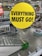 A yellow circular sign with black text saying 'EVERYTHING MUST GO!' is prominently displayed in the center. In the background, there is an indoor retail store setting with shelves, a staircase, and shopping carts. Several other sale signs are visible in the distance, indicating that the store is likely closing down.