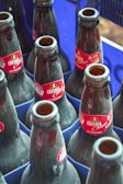 Several empty dark glass bottles with red labels are placed within a blue plastic crate.