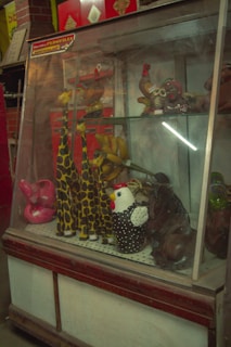 A display case contains a variety of colorful animal figurines. These include several giraffes with a giraffe pattern, a hen with polka dots, and other whimsical animal figures. The setting appears to be eclectic and vibrant.