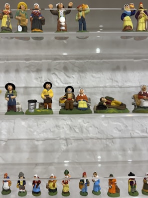 Collection of delicate porcelain figurines arranged on a glass shelf.