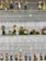 A display of small ceramic figurines arranged on shelves, depicting various characters in traditional attire. The figures are in rows on transparent shelves against a textured wall, featuring a range of vibrant colors and intricate details in their costumes and poses.