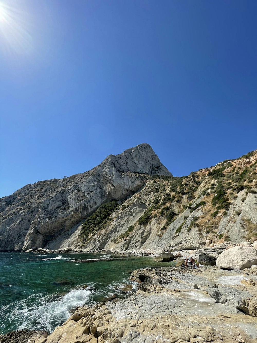 a rocky beach with a body of water and a mountain in the background