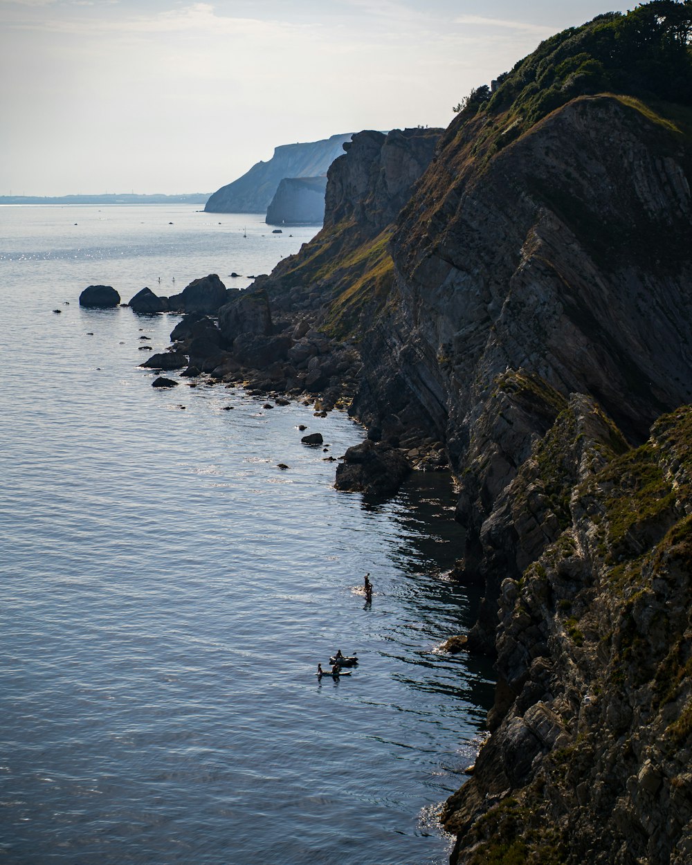 a group of people swimming in the ocean by a cliff