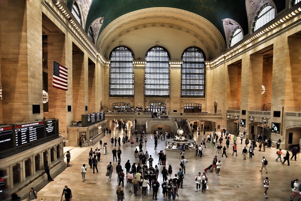 a large group of people in a large building with a flag on the ceiling with Grand Central Terminal in the background