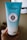A blue tube of L'Occitane body scrub is held in a hand. The tube features the label 'Gommage Riche Corps' with 10% shea butter indicated. The background is softly blurred, highlighting the product.