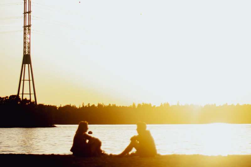 couple sitting on a beach facing a tower