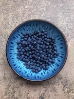 Close-up of a deep blue stoneware bowl filled with fresh berries on a rustic wooden table.