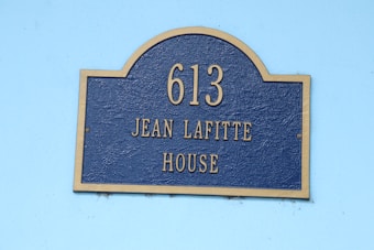 A rectangular sign with a rounded top displaying the number 613 and the name Jean Lafitte House. The sign is blue with a gold border and gold lettering.