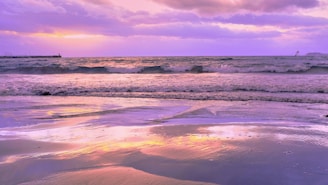 A serene beach at sunset with gentle waves and a colorful sky reflecting on the water.