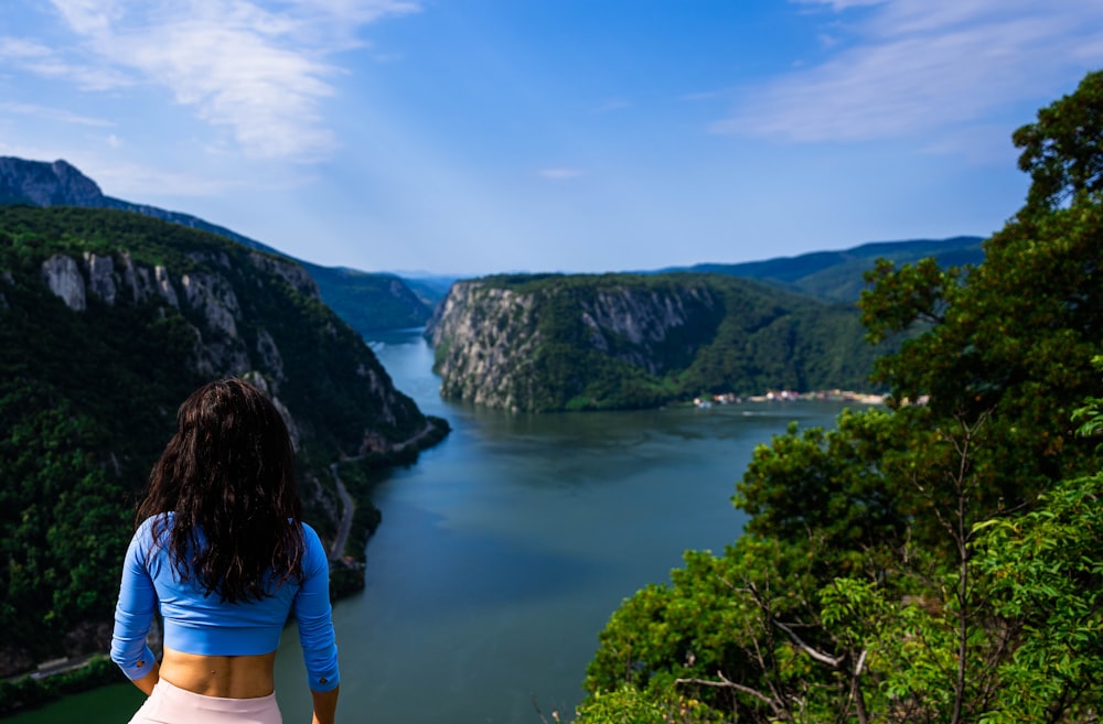 a person looking at a body of water with trees and mountains in the background