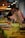 Two people, possibly participating in a painting workshop, are positioned near easels on a table that is set up for an art activity. The table is adorned with glasses containing a pinkish drink, paintbrushes, and art materials. Warm lighting adds a cozy ambiance to the setting.